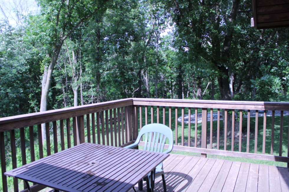 Cabin back patio including a metal table and plastic Adirondack chairs overlooking the woods