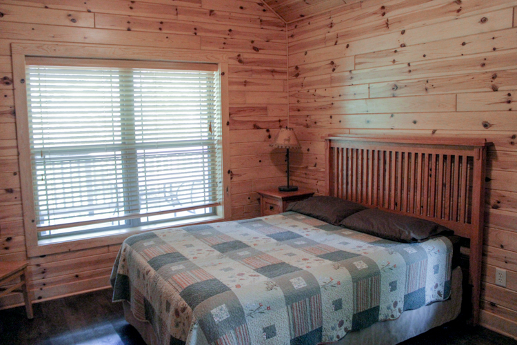 Cabin 3 2nd bedroom with queen-sized bed and quilt on a mission wood bedframe, night stand and lamp,