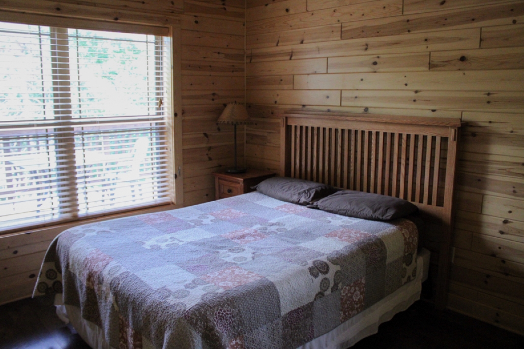 cabin 1 view of the bedroom including queen bed with quilt on a mission wood bedframe, along with a 