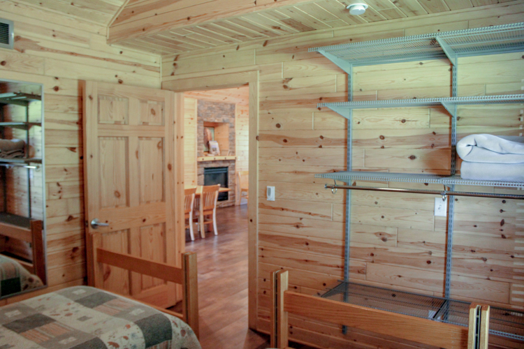 Cabin 3 alternative view of bedroom 1 showing mounted shelving and door that leads out to fireplace/