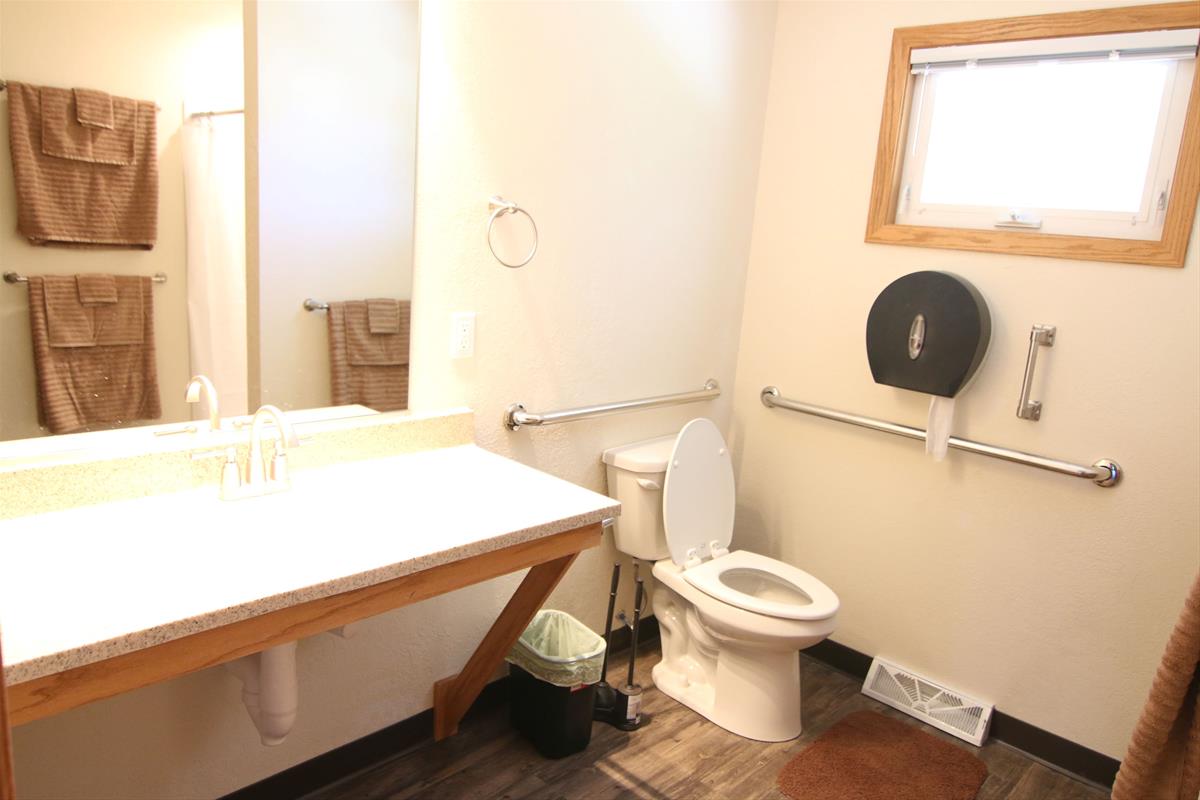 Bathroom with toilet, sink, towels, and small window with logs of natural light